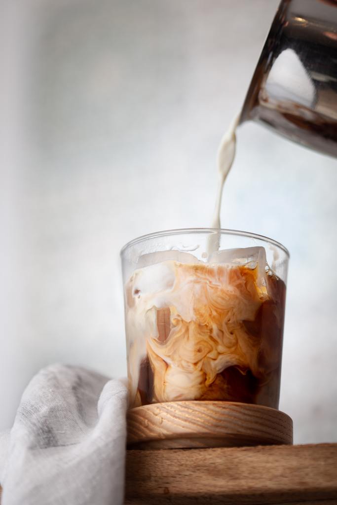 pouring mile into glass of iced coffee